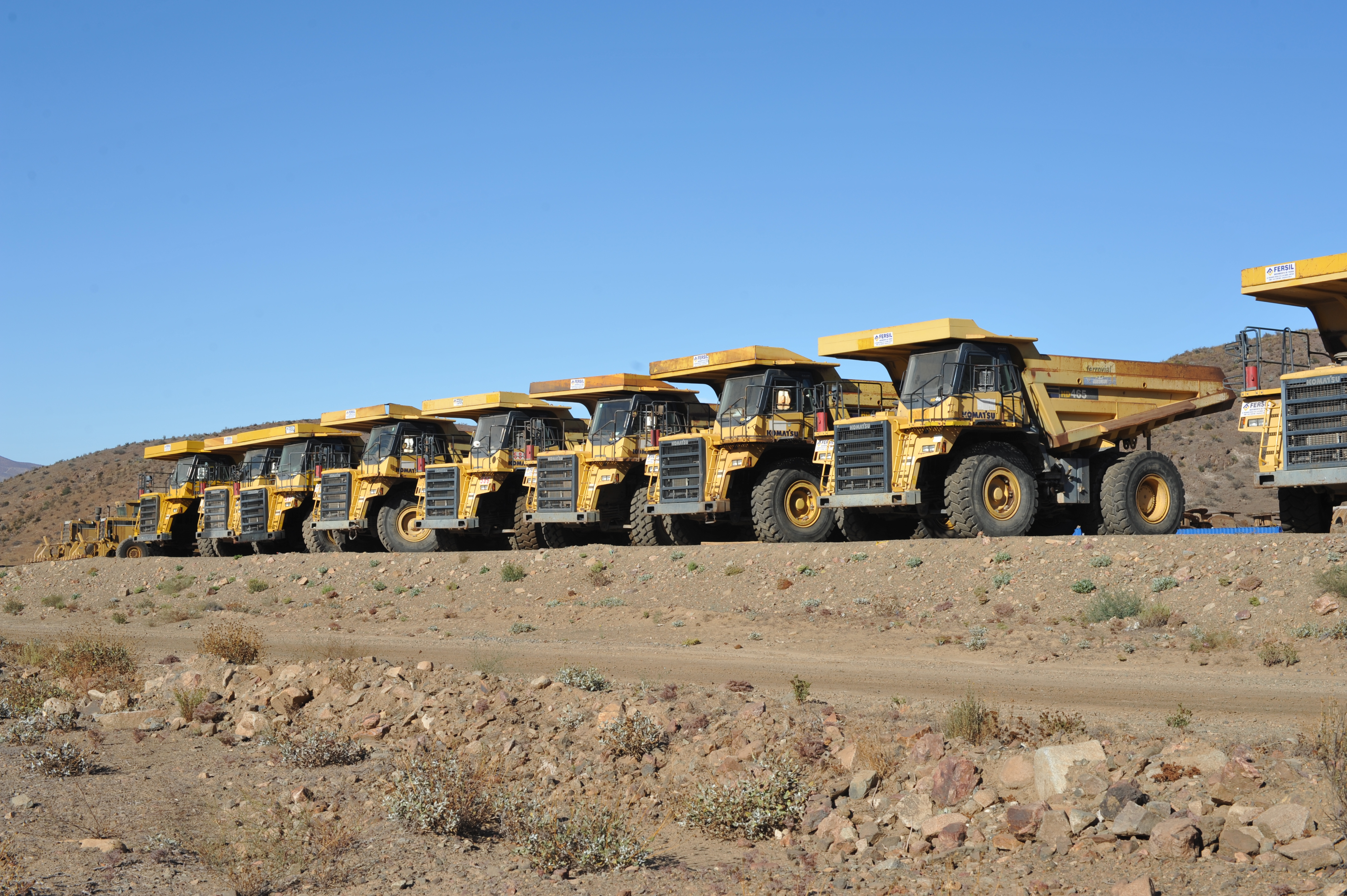 A lineup of large haul trucks at an open-pit mining site.
