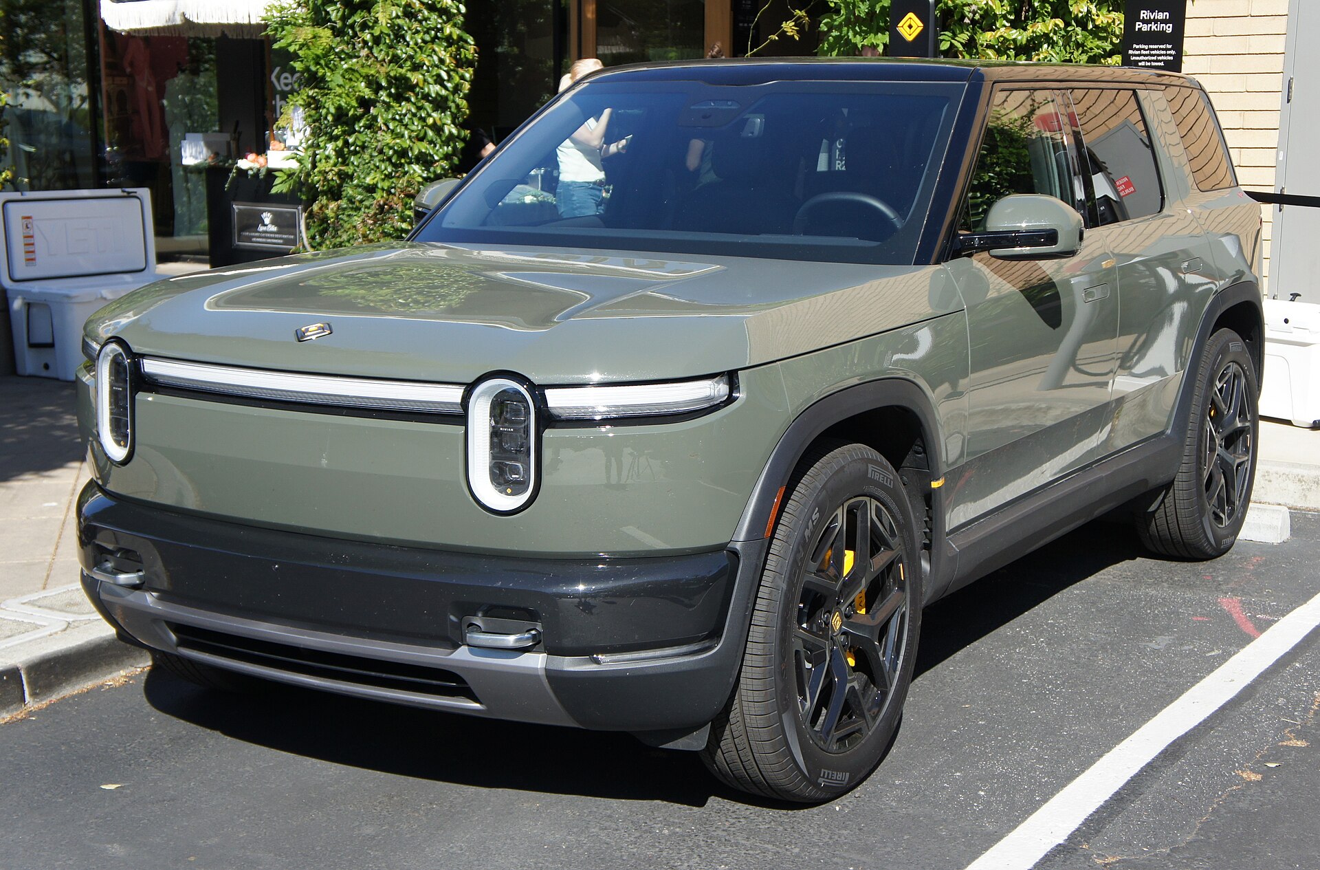 A Rivian R2 in Launch Green parked outside a Rivian Space retail location.